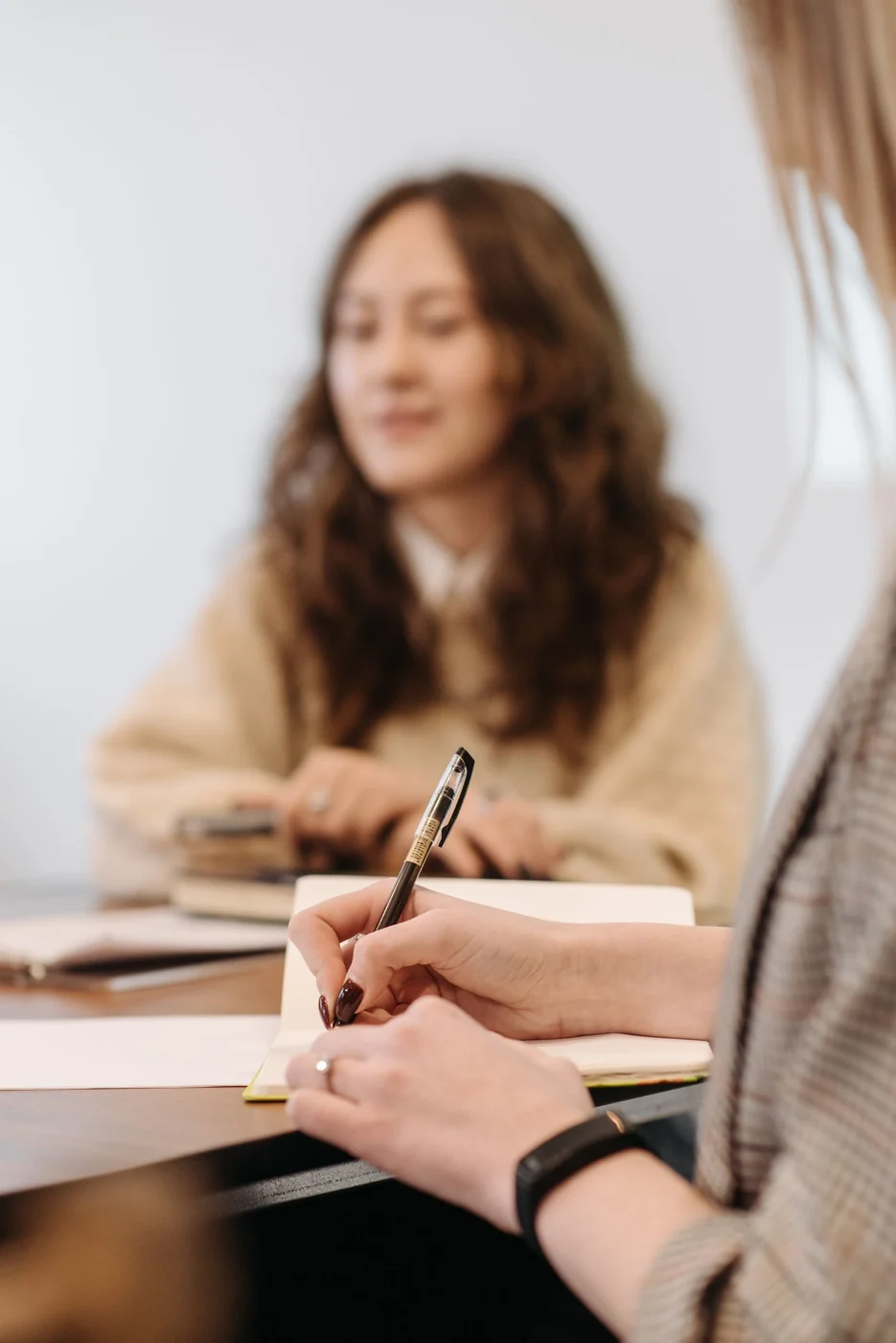A participant writes notes in a notebook during a meeting.